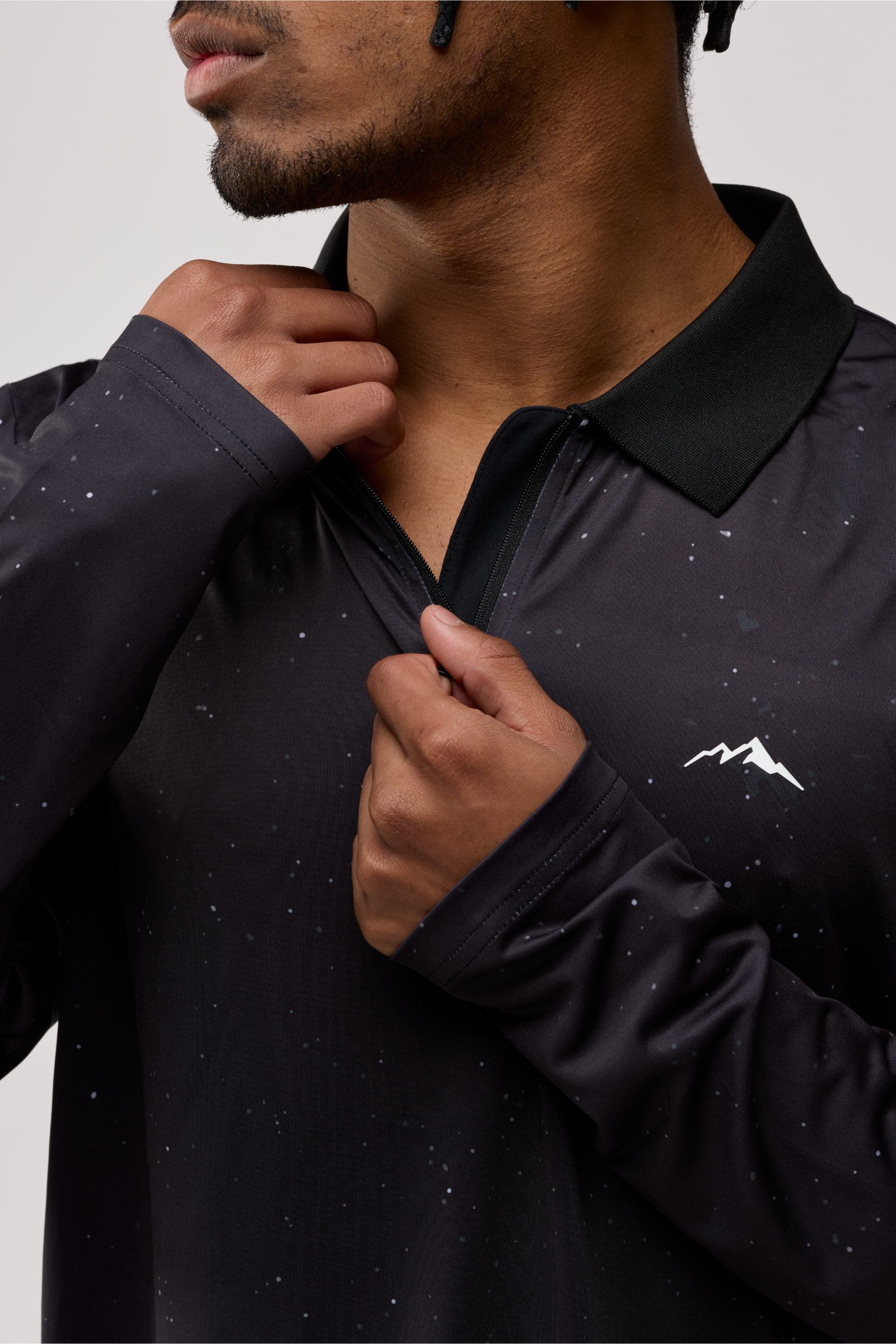 Person wearing a black long-sleeve shirt with a mountain logo on a plain background