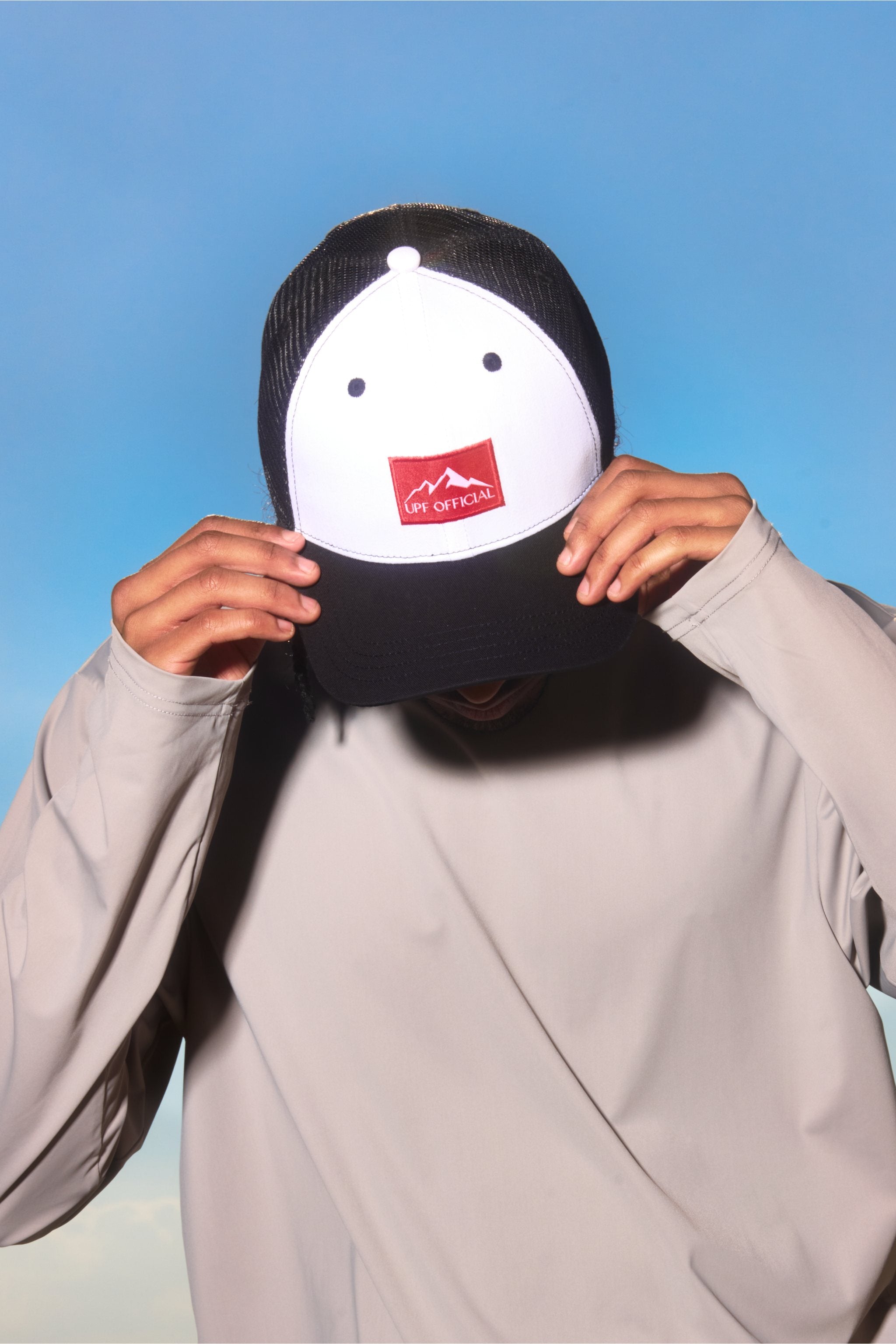 Person holding a black and white cap with a red logo against a blue background