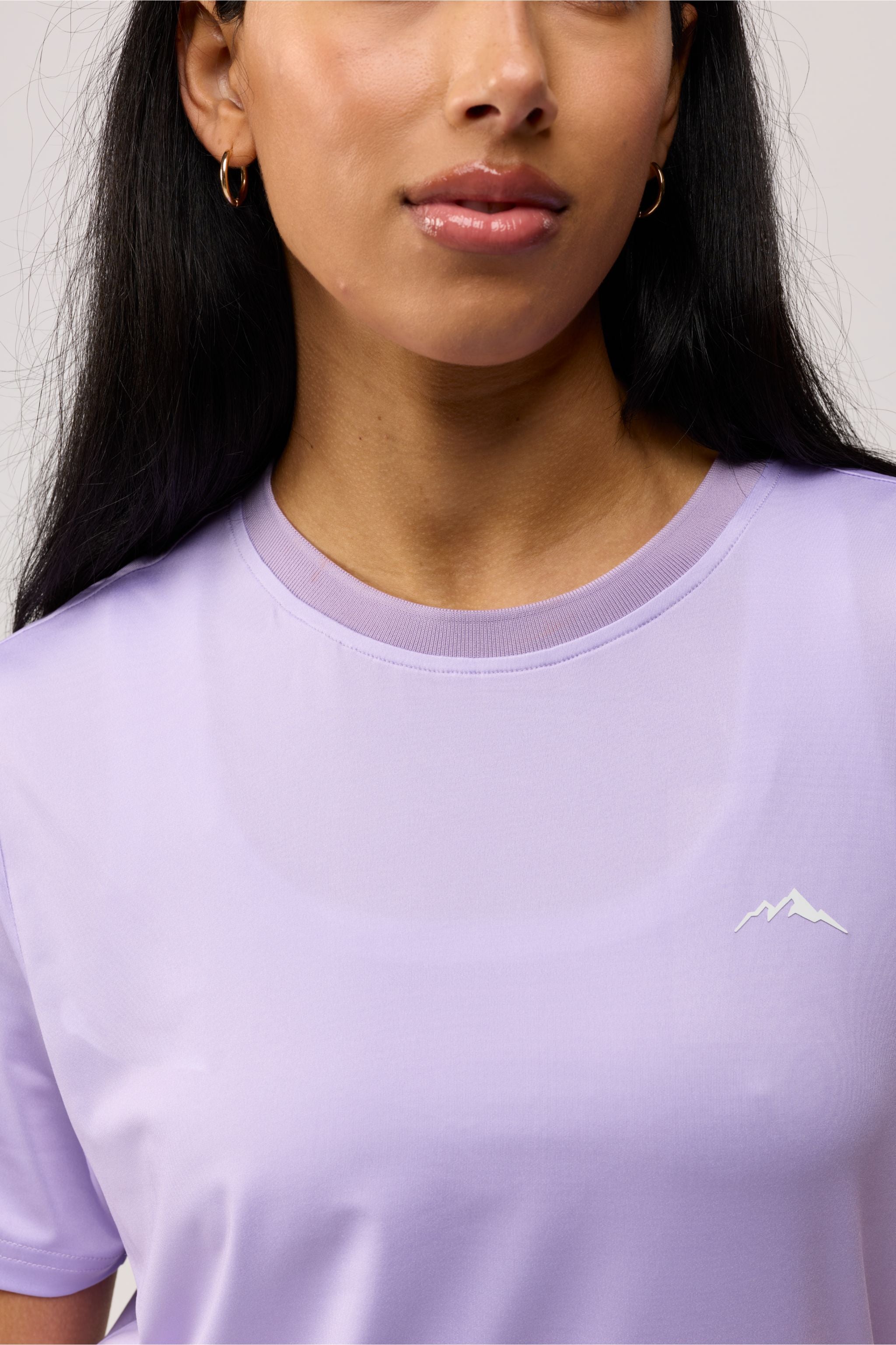 Person wearing a lavender t-shirt with a small logo on chest